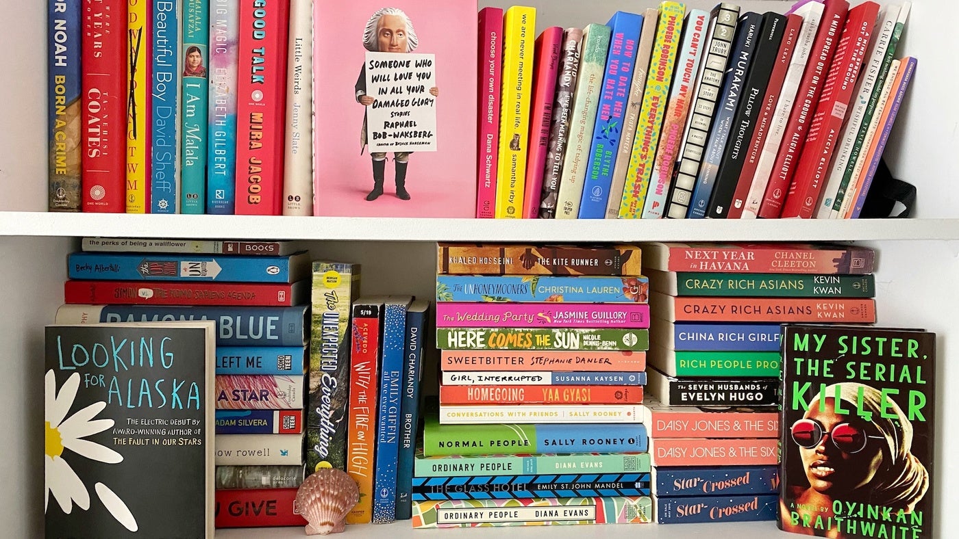 White bookshelf with vertical and horizontal stacks of multi-colored mystery books like "Looking for Alaska" and "My Sister, the Serial Killer."