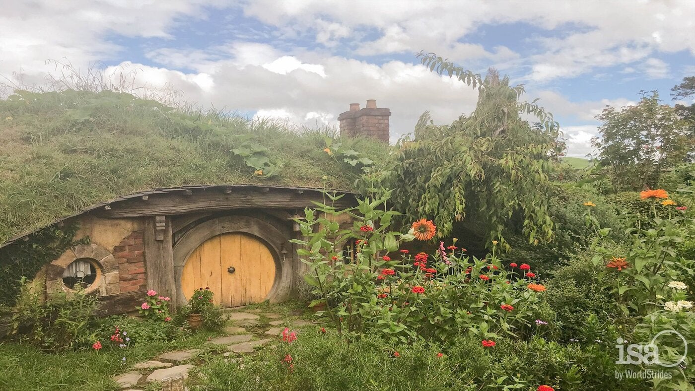 Small hobbit house with a window door covered in greenery, flowers, and foliage.
