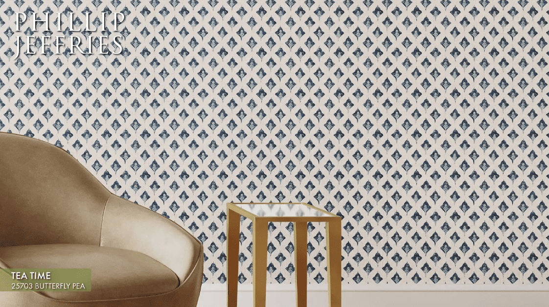 Phillip Jeffries wallpaper with a cream background and blue diamond-shaped print behind a brown leather chair and accent table.