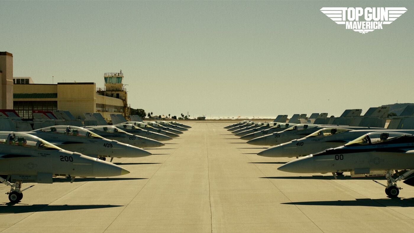 Air carrier hanger with fighter pilots lined up and the "Top Gun Maverick" logo in the upper right-hand corner.