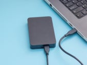 Black external hard disk connecting to a laptop on a blue background.