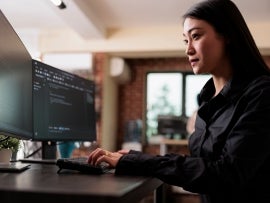 Woman in a black shirt in front of a computer with two monitors.