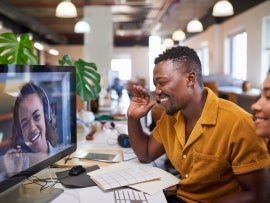 A Black man waves to his colleague on a video call from his office