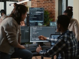 Programer sitting on desk discussing with mixed team of software developers about artificial intelligence.