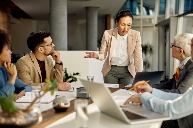 Asian female leader using laptop and communicating with her business team during meeting in the office.