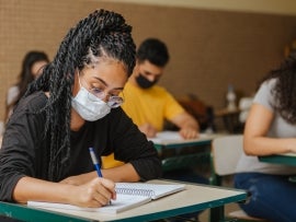 Latin students in the classroom. female student with twisted hair wearing mask and writing in notebook with a pen. Covid-19. Pandemic.