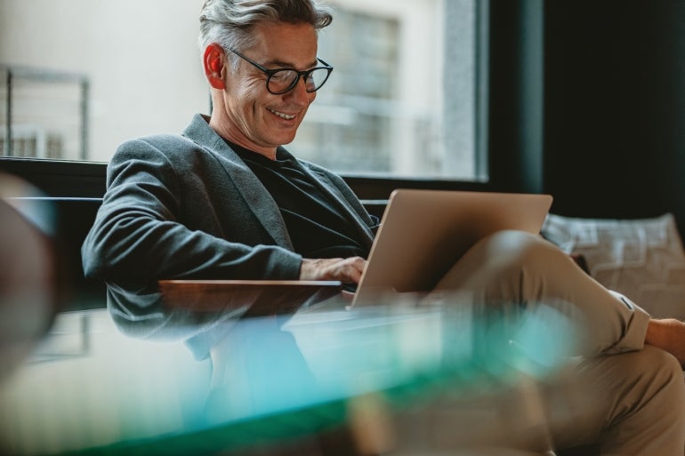 Smiling businessman sitting in office lobby working on laptop. Male business professional working in office lobby.