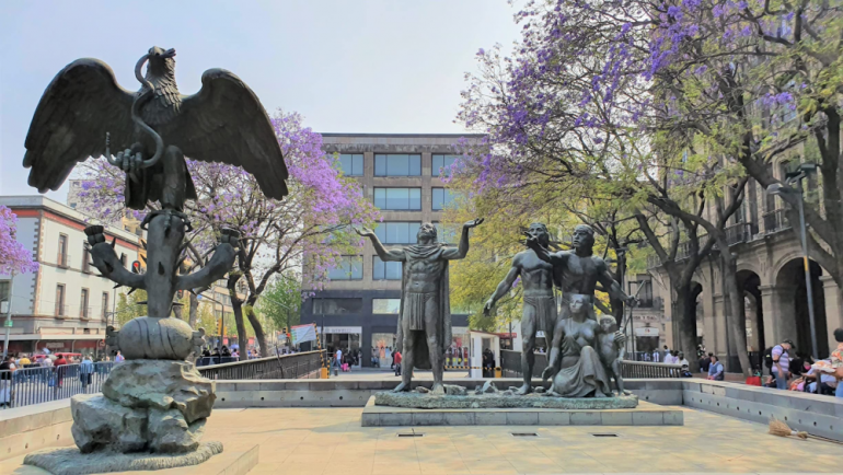 Statues surrounded by purple flowering trees in a courtyard in Mexico City
