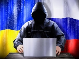 Anonymous hacker working on a laptop, flags of Ukraine and Russia