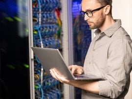 man holding an open laptop next to networking infrastructure