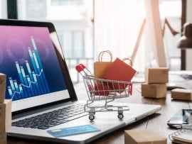 Shopping bags in shopping cart and credit card on laptop with paper boxes on table and sales data economic growth graph on screen, buying and selling services online on network, online shopping and e-commerce concept.