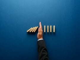 Businessperson stopping falling dominos with their hand.