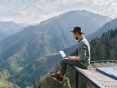 Young man freelancer traveler wearing hat anywhere working online using laptop and enjoying mountains view.