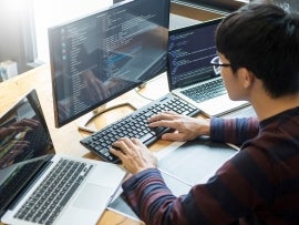 a person coding on a computer with a laptop open on either side of the monitor