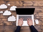 A small business owner typing on a laptop with cloud symbols floating up from the computer.