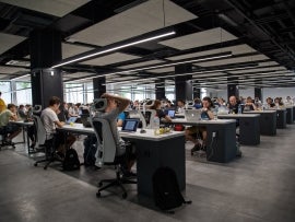 Many tech workers showing focus and stress in a large open office.