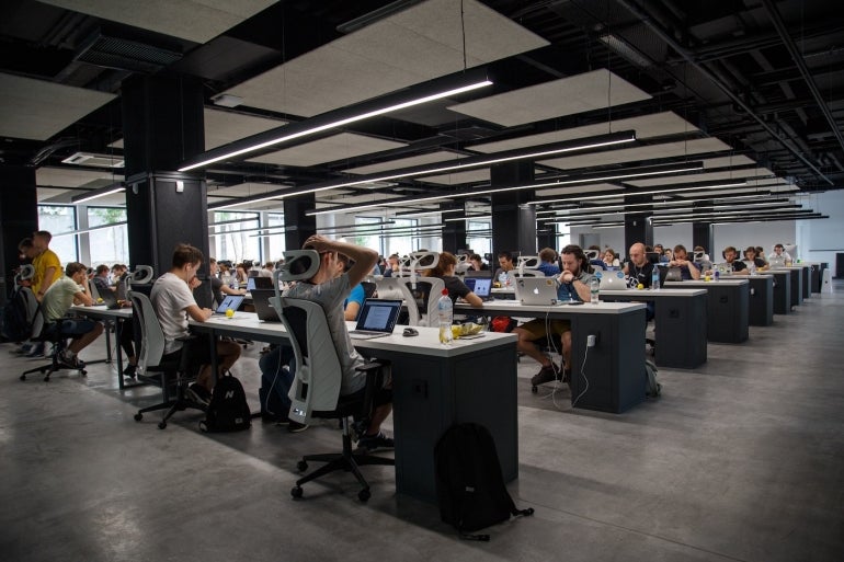 Many tech workers showing focus and stress in a large open office.