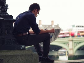 A person reading tech news by a bridge.