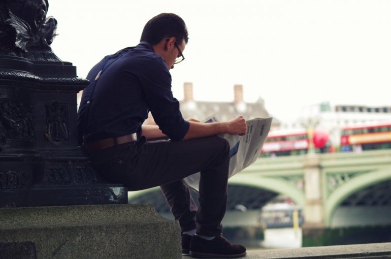 A person reading tech news by a bridge.