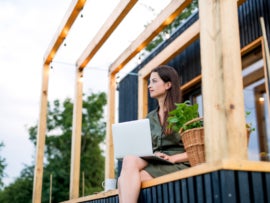 Young woman with laptop outdoors, weekend away in container house in countryside.