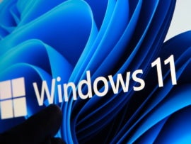 Windows 11 logo seen on the screen of tablet and user pointing at it with finger.