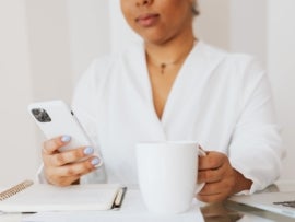This photo shows someone view a mobile phone and drinking coffee.
