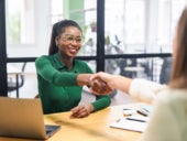 Two women shaking hands in a boardroom.