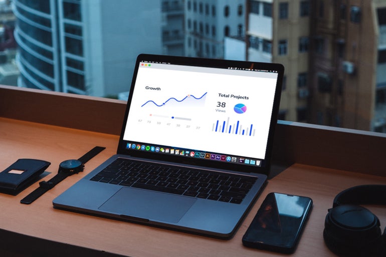 Open laptop displaying graphs and charts, with a wallet, a watch, a mobile phone, and headphones on the side.