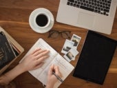 Woman studying notes with coffee and laptop on table.