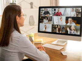 Woman sitting at a desk in front of a computer screen attending a video meeting with a group of other people.