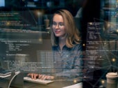 Woman programming on her desk with code blocks on virtual screen.