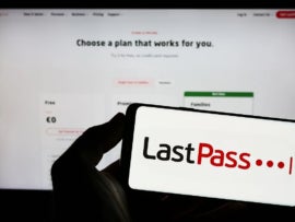 Person holding a smartphone with LastPass app and a LastPass pricing webpage in the background.