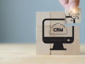 Hand hold wooden cubes with AI-CRM icon on grey background.