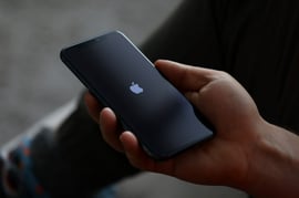 Person holding an iPhone displaying the Apple logo on its startup screen.