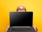 Expressive young man in glasses giving innovative laptop making presentation on yellow background.