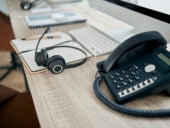 A headset placed on a call center desk, near a landline phone.