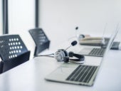 Laptops on a shared desk with headsets and other equipment.