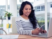 Smiling woman using smartphone and laptop.