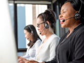 Friendly black woman wearing microphone headset working in call center with international team as telemarketing customer service agents.