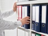 Office staff placing a blue folder on a shelf full of filing folders.