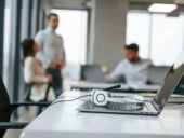 A headset set on the keyboard of an open laptop in an office setting.