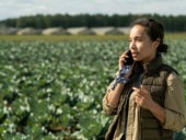 A woman talking on a phone beside a field.