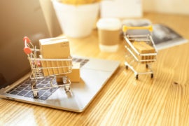 Brown paper boxs in a shopping cart with laptop keyboard on wood table with office background.