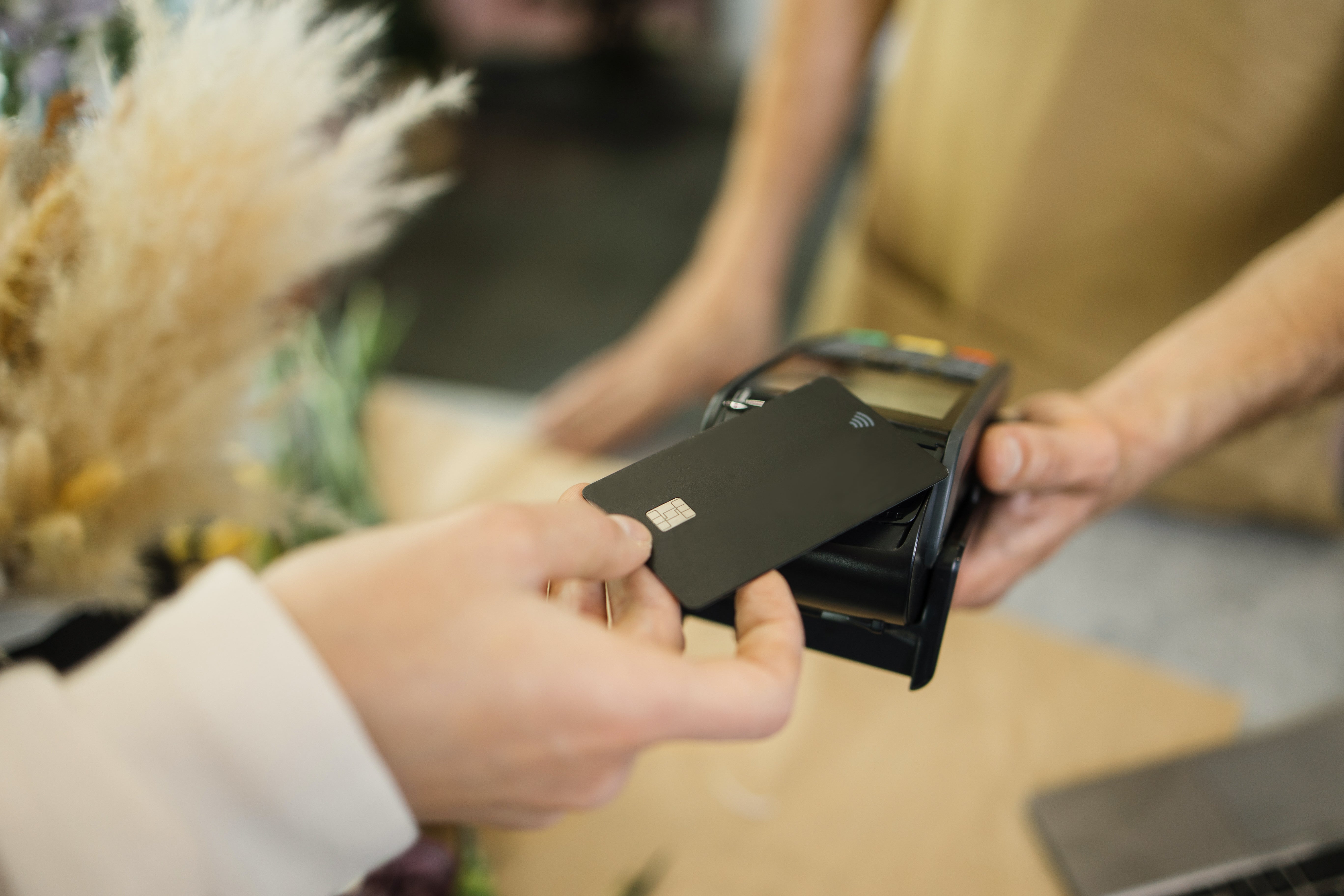 Close-up shot of unrecognizable male customer paying for her purchases with credit card in flower shop, blurred background