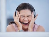 Stressed woman holding head wearing headset in call centre