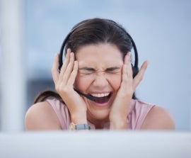 Stressed woman holding head wearing headset in call centre