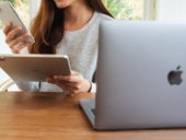 A woman holding and using Apple devices on a desk.