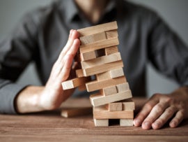 Businessman holds falling structure made from wood blocks.