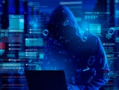 Hooded computer hacker using a laptop surrounded with virtual data.