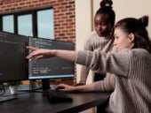 Two developers discussing a programming code on display monitors.